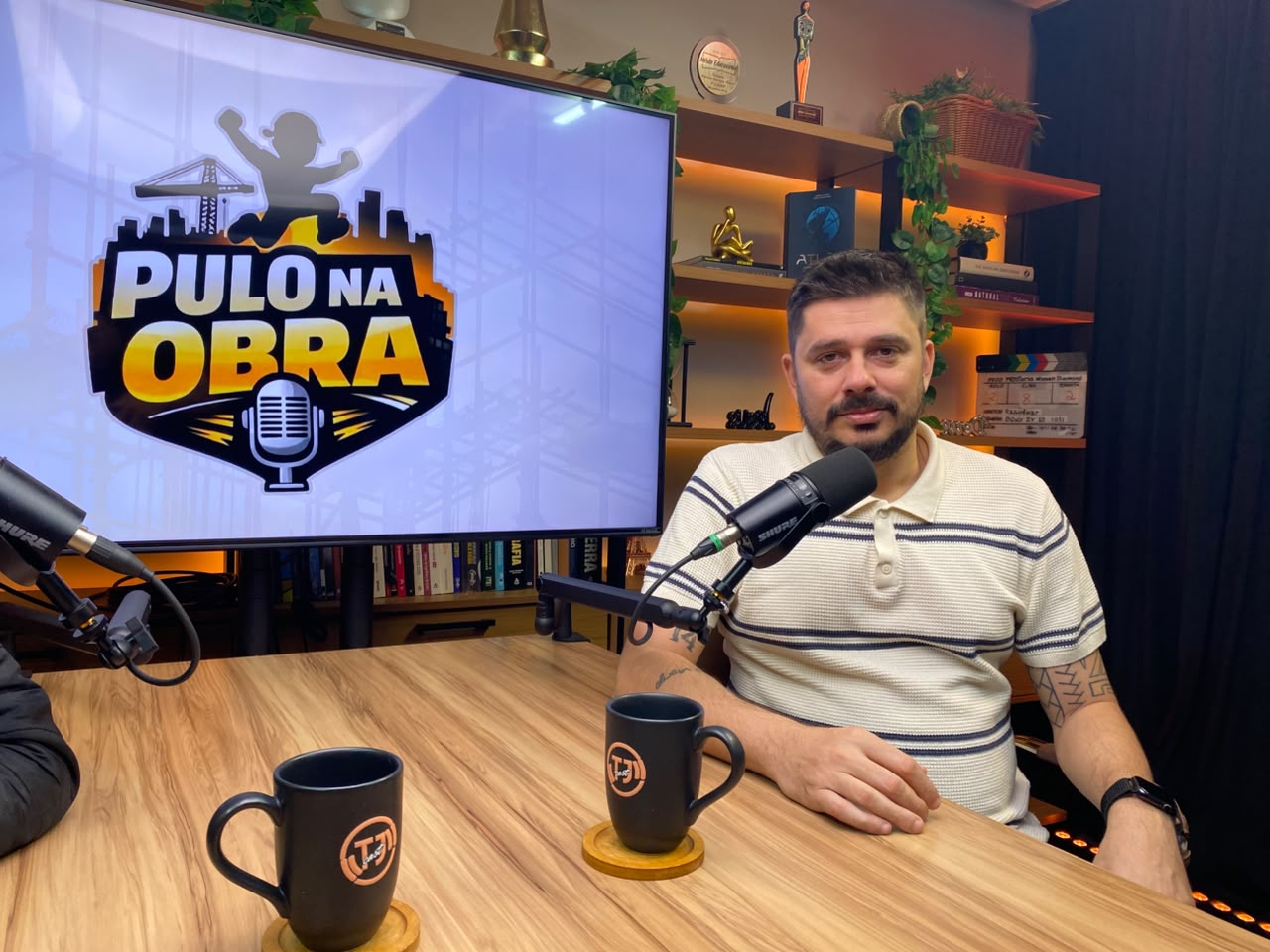 Estúdio do podcast Pulo na Obra: apresentador ao microfone e a logo do programa na TV ao fundo