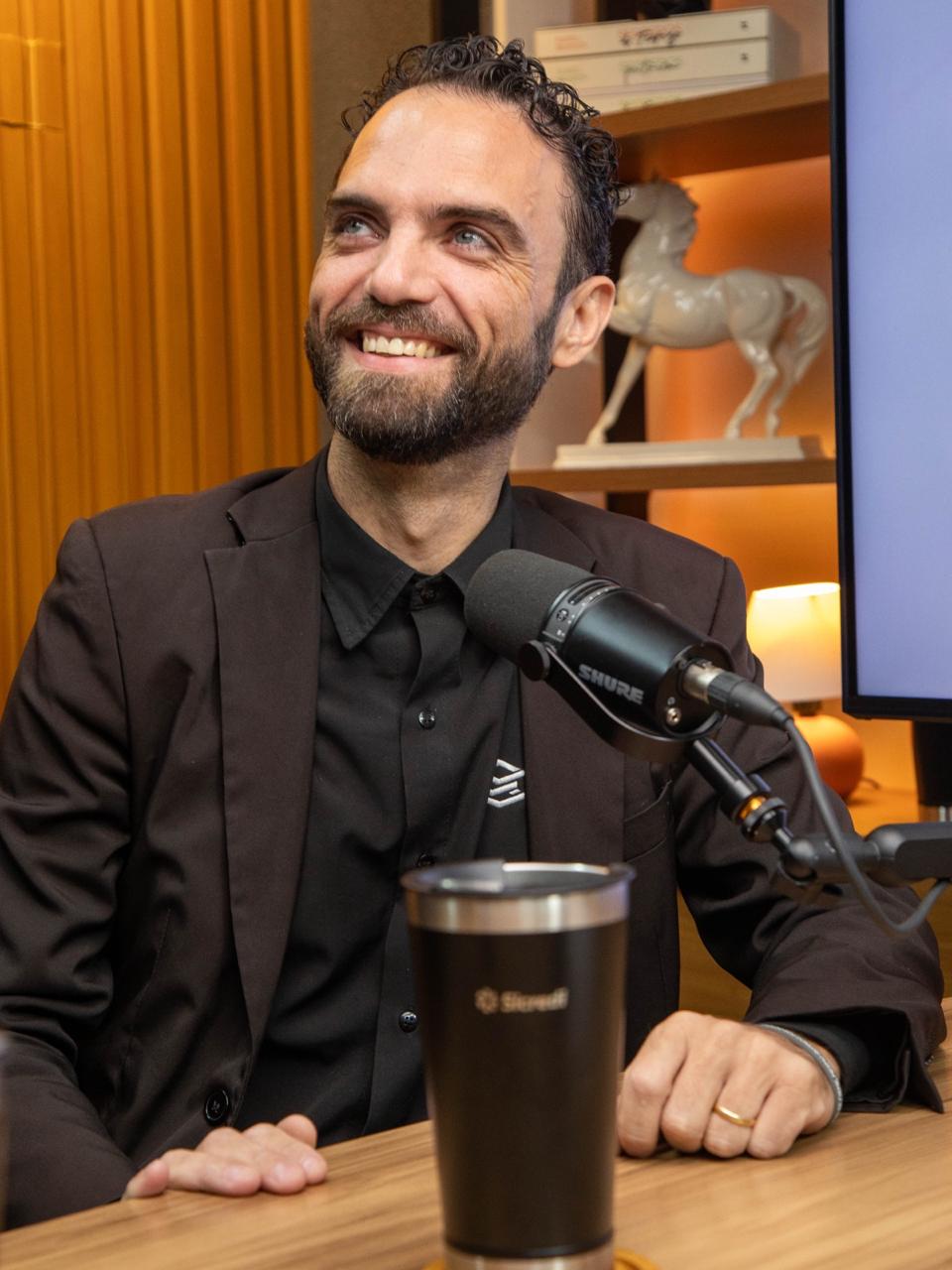 Rodrigo Jose Pereira, apresentador do Pulo na Obra, rindo durante a gravação, com pin da RDX na lapela