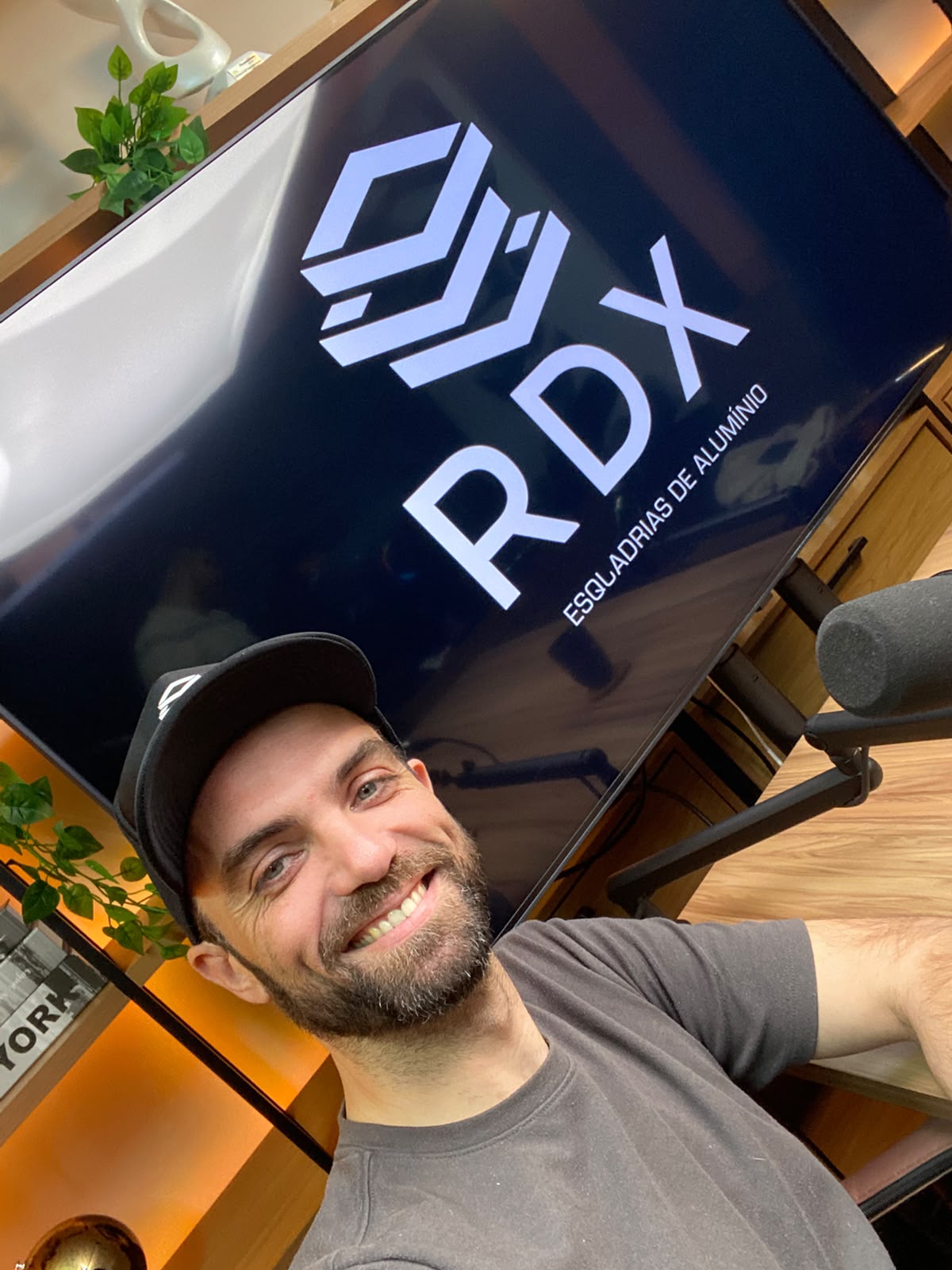 Apresentador do Pulo na Obra em frente à TV do estúdio exibindo a logo da RDX Esquadrias de Alumínio